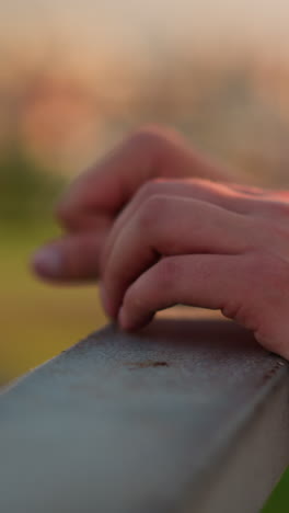 vista en primer plano de la mano de una persona blanca descansando en una barandilla de hierro con banda de muñeca negra en la mano derecha, fondo borroso con efecto de luz bokeh con colores cálidos