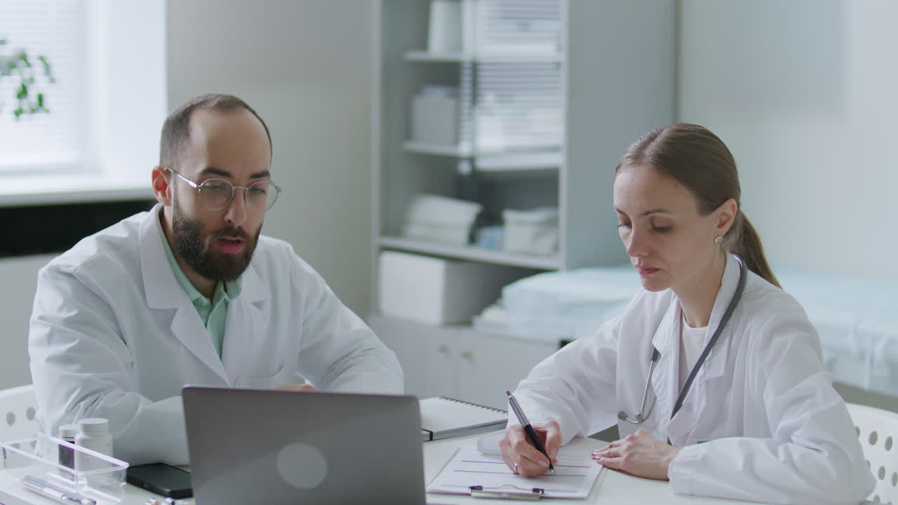Two Doctors Reviewing Patient Information on Laptop at Work in Clinic