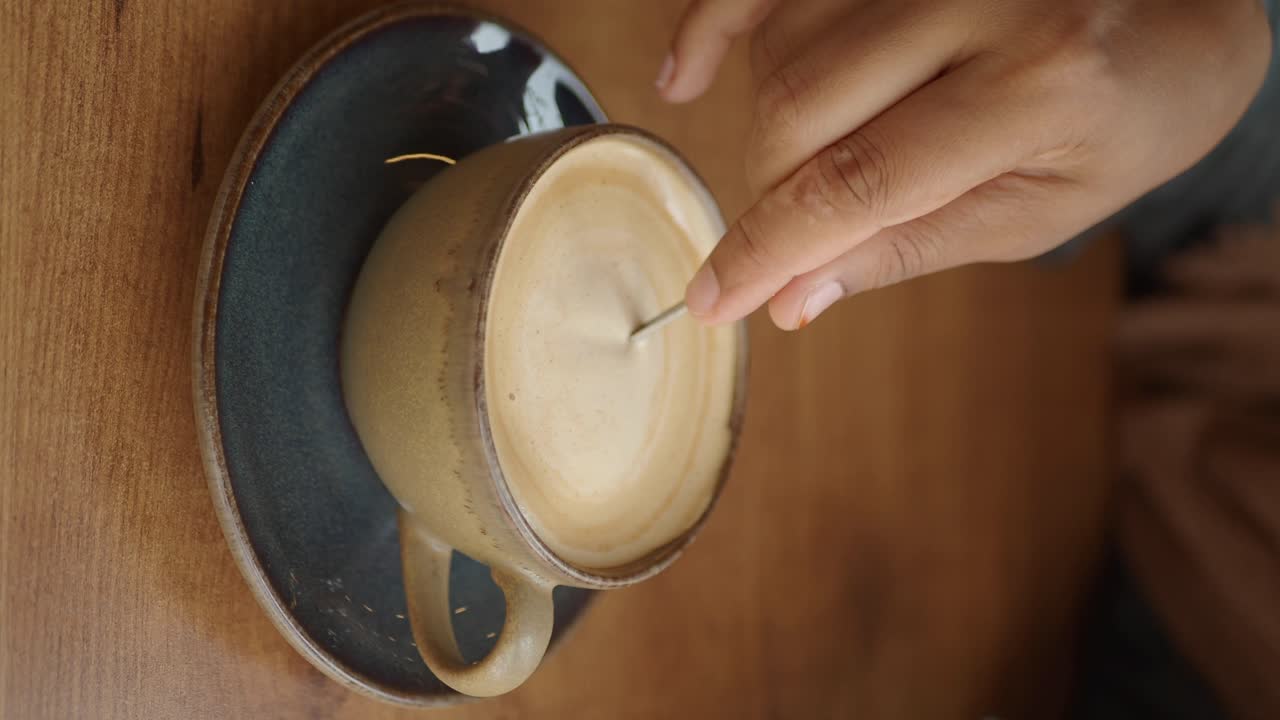 A hand stirring a latte in a ceramic cup