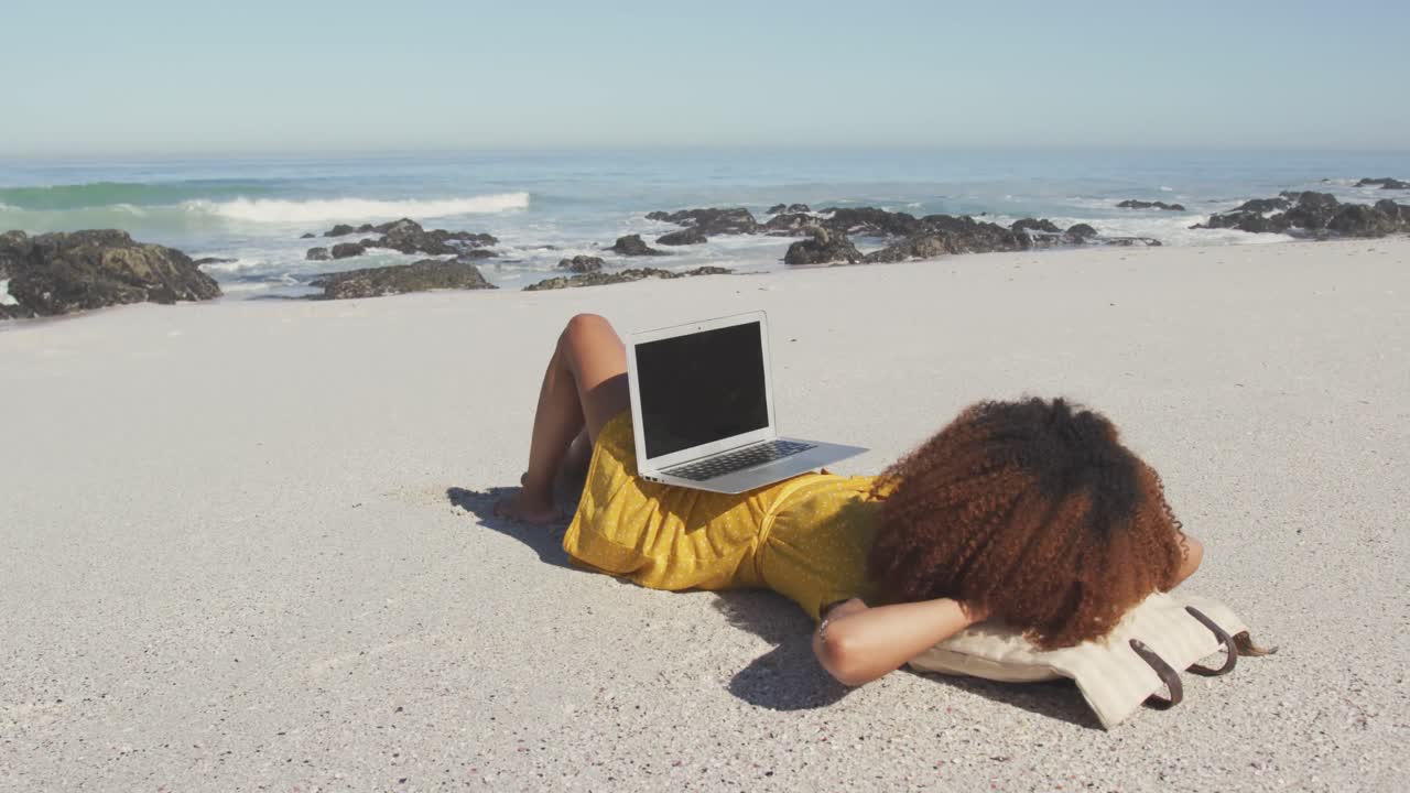 mujer afroamericana con su computadora portátil en la playa