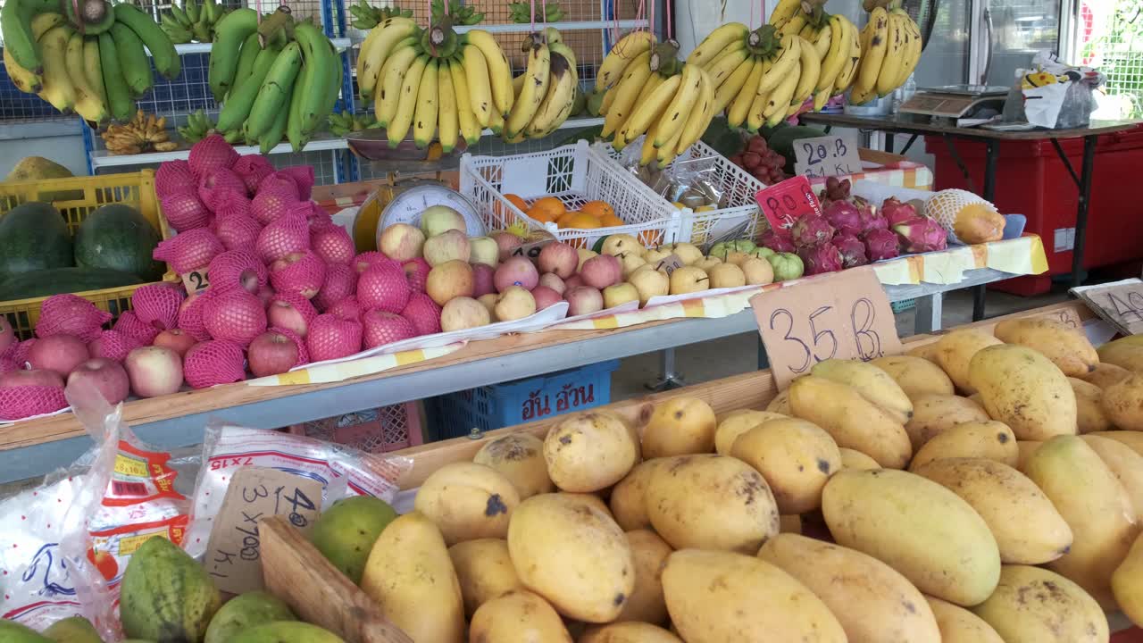 Frutta fresca su una bancarella del mercato con manghi thailandesi, mele e banane, con panoramica lenta da sinistra a destra in Thailandia.
