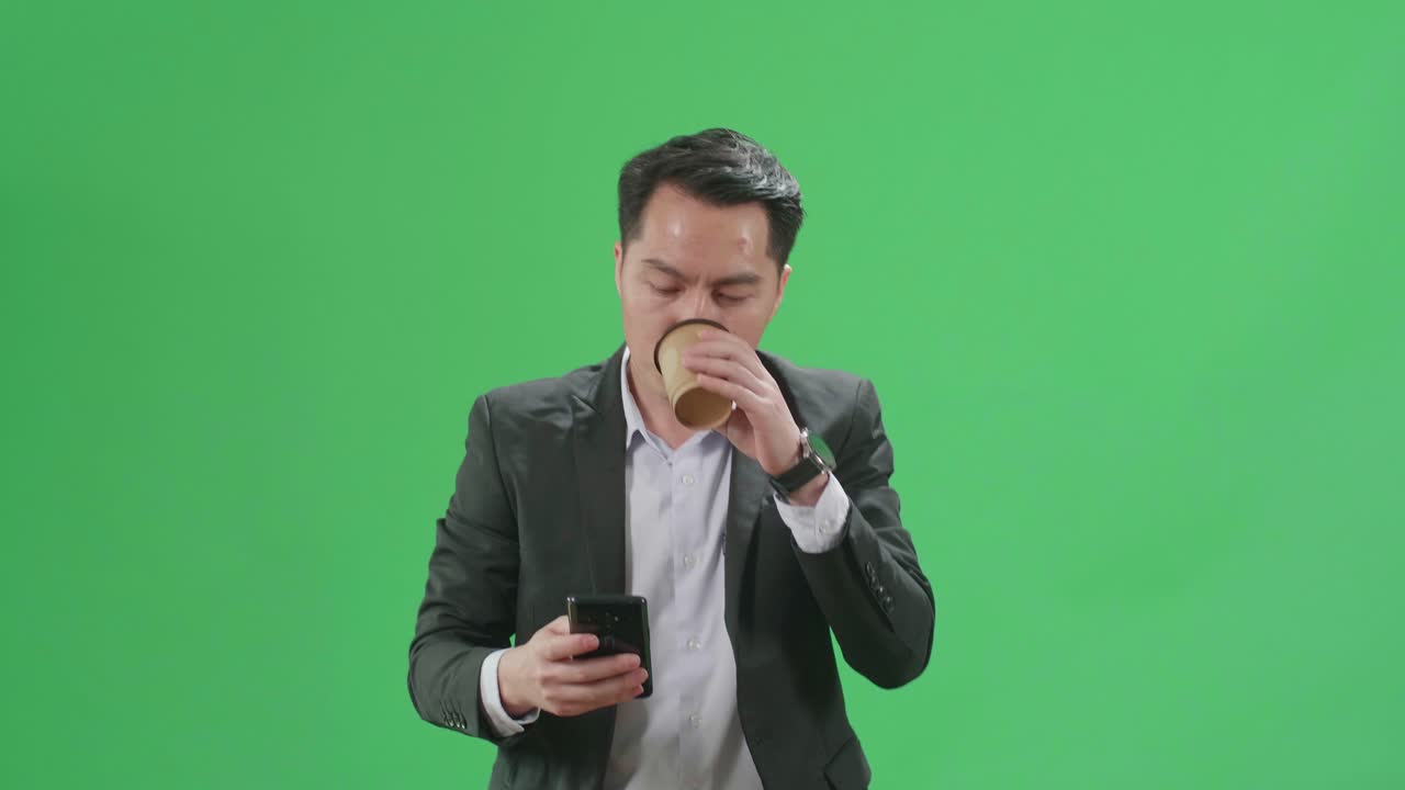 Asian Business Man Use Mobile Phone And Drink Coffee While Walking On Green Screen Chroma Key