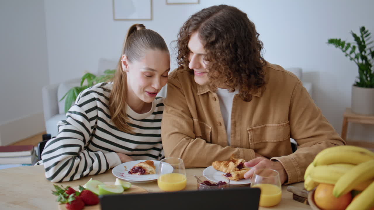 Breakfasting couple looking laptop in modern kitchen closeup. Relaxed man woman