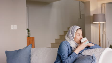 Mujer-Birracial-Feliz-Con-Hijab-Bebiendo-Té-En-El-Sofá-De-Casa-Con-Espacio-Para-Copiar,-Cámara-Lenta