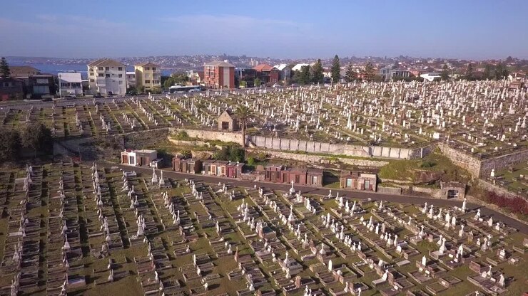 Volo sopra un cimitero verde nella periferia dell'Australia con un progetto di costruzione nella scena, ripresa inversa.
