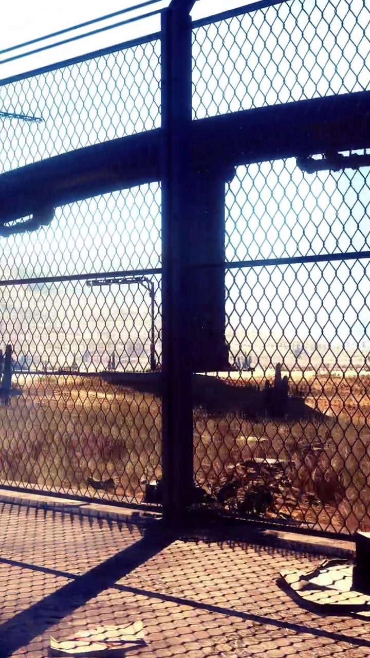 Sacco della spazzatura vicino a una recinzione metallica con una struttura a ponte e un paesaggio in lontananza.