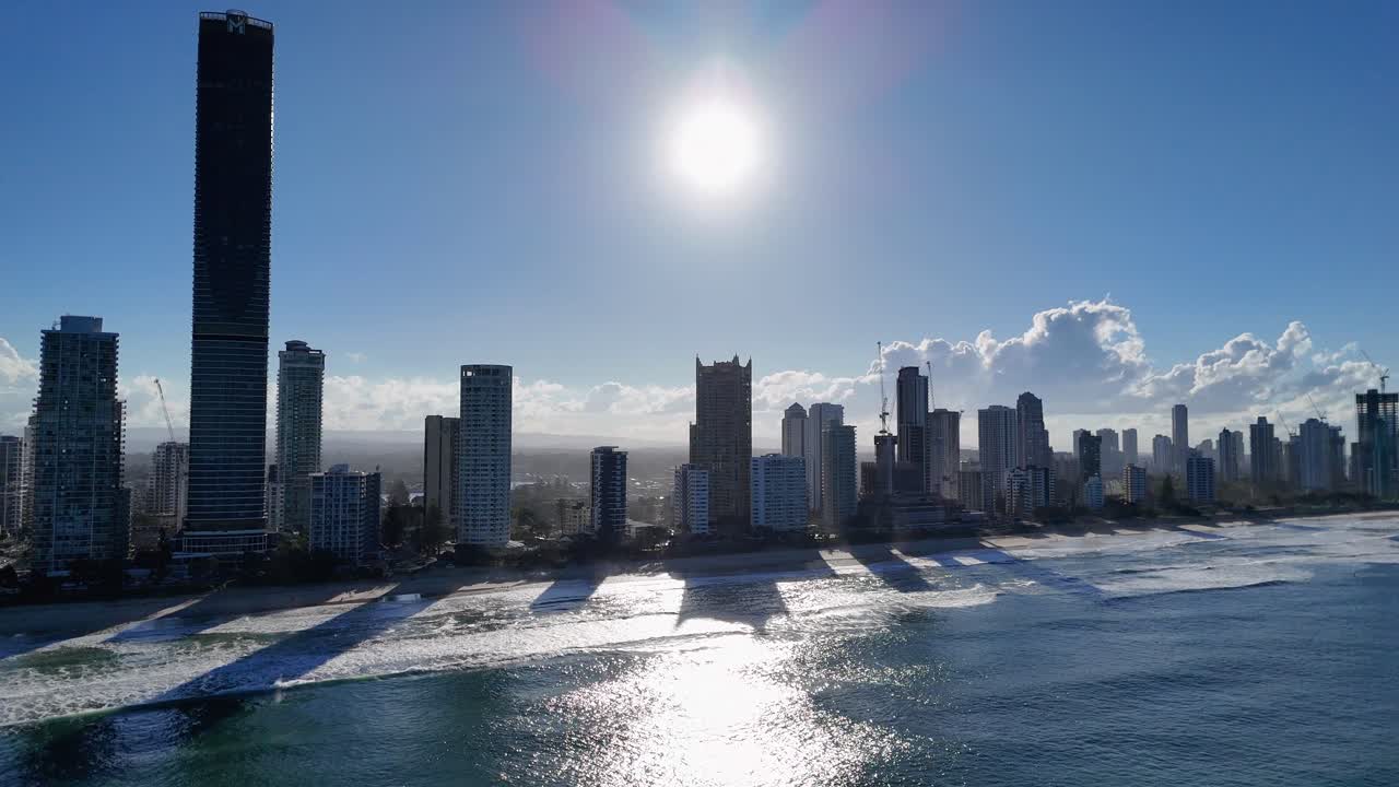 Drone captures Gold Coast skyline with sun setting over ocean, highlighting skyscrapers and shimmering water reflections