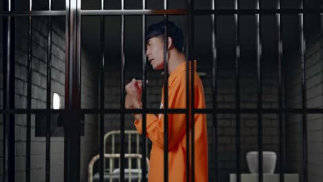 side view of asian male prisoner in handcuffs standing in prison, pointing fingers at himself and shaking his head in anger doubting about something
