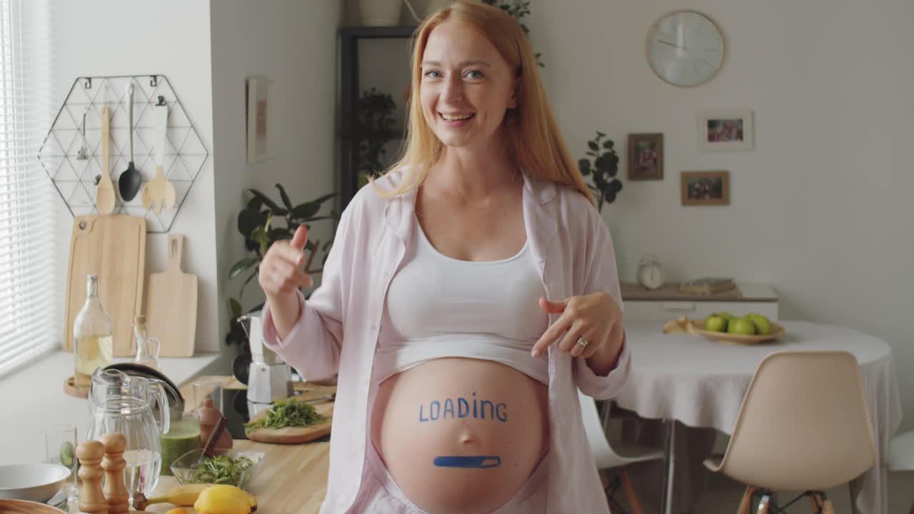 Mulher grávida engraçada com 'Loading' na barriga na cozinha