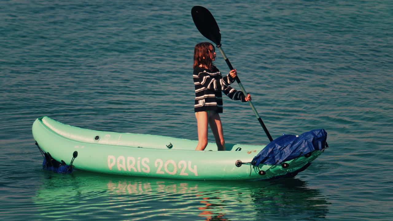 Antibes, France - April 5, 2025: Girl standing in a mint green inflatable kayak, using a double-bladed paddle to move across the water