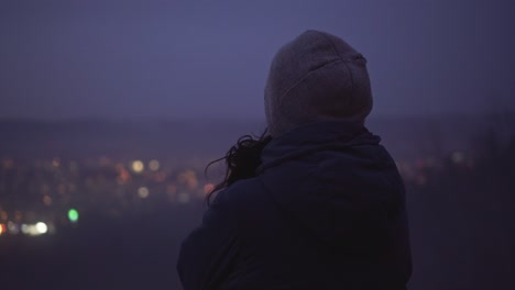 female watching blurry city lights and thinking about life, middle back view