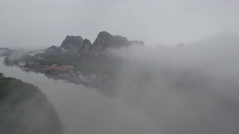 fotografía aérea a través de nubes de niebla sobre el parque nacional ao phang na con vistas a manglares y acantilados de piedra caliza