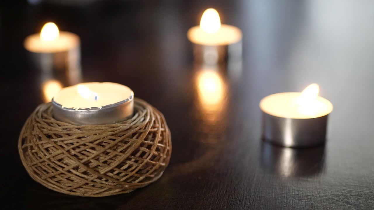 una pequeña vela decorativa y mecha de cáñamo con las llamas de muchas más velas parpadeando y ardiendo en el fondo
