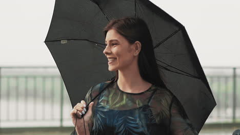 smiling woman with black umbrella stands under light rain