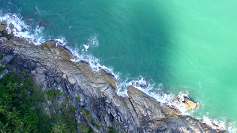 drone flotando sobre la línea diagonal costa costa en tailandia agua turquesa rompiendo las rocas cerca de palmeras moviendo la sombra del sol lenta aproximación al agua hermoso paisaje aéreo