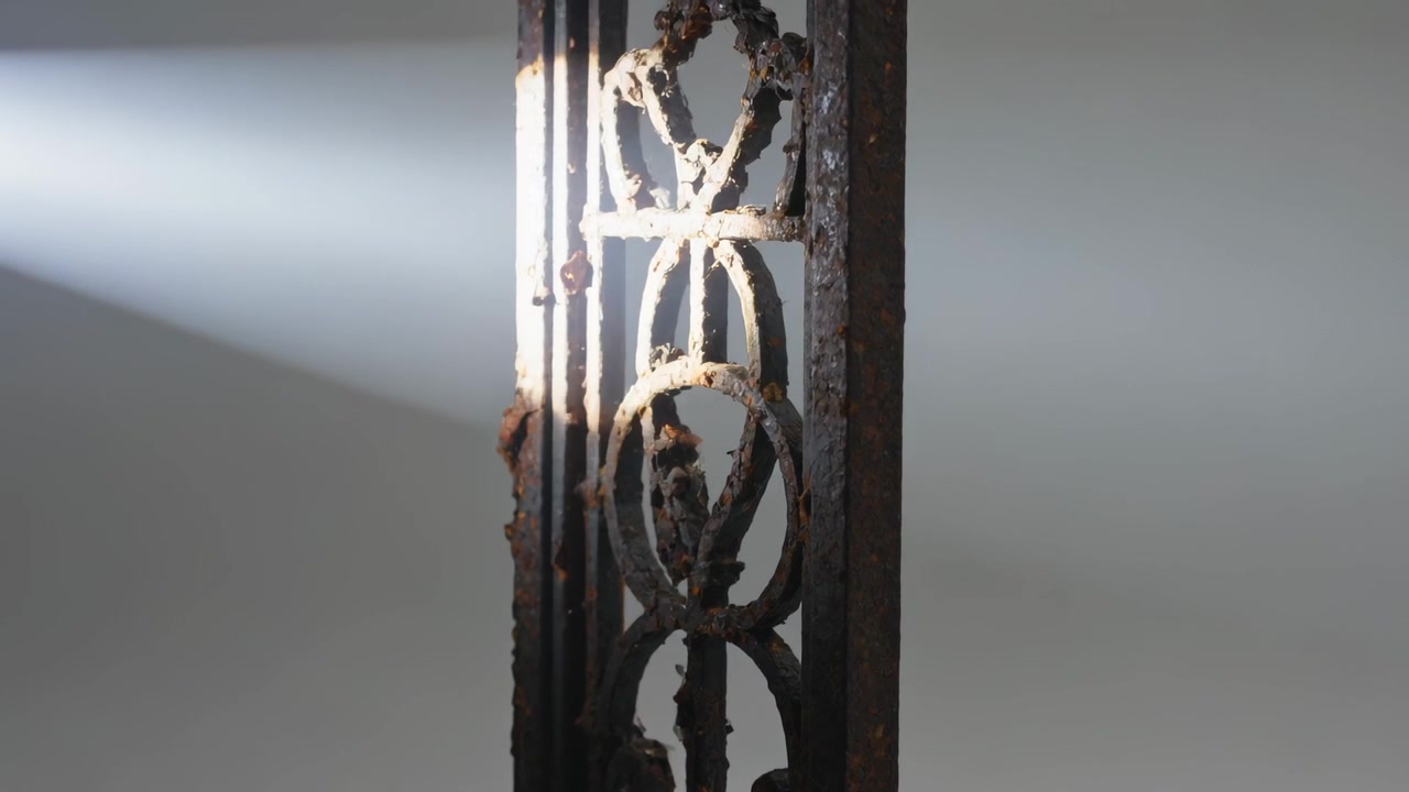 Luce solare che entra formando un raggio diagonale che sfiora una colonna metallica decorativa nella stanza, rivelando ruggine.