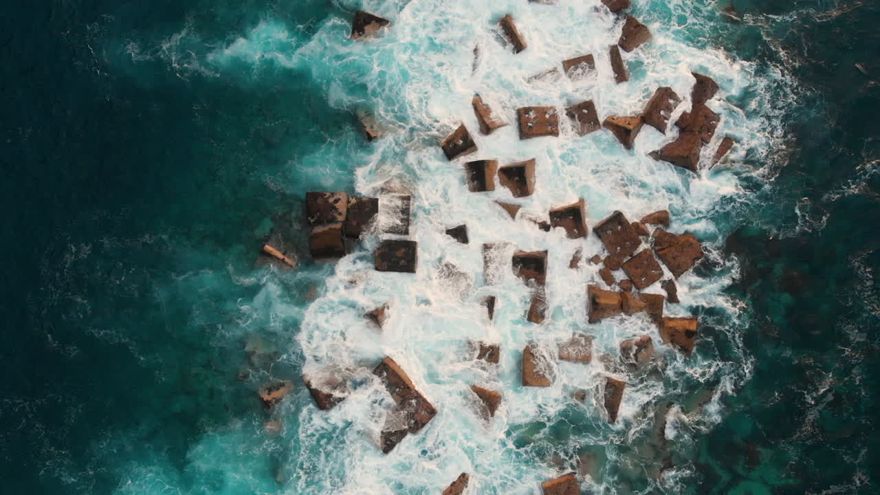 Top view Steep volcanic shore, reefs of volcanic lava, stormy ocean, white foam from the giant waves that hit rocks. Aerial shot. Garachico, Tenerife, Canary Islands.