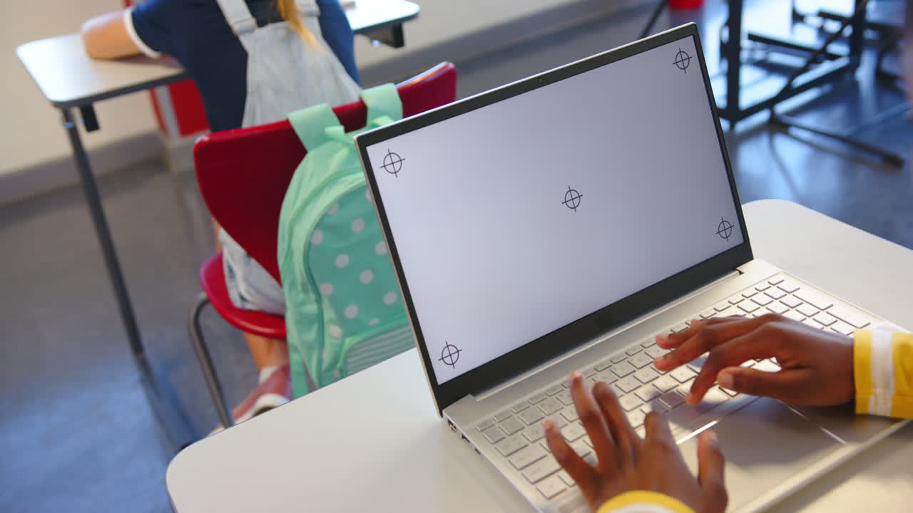 Using laptop, student working in school classroom with backpack on chair