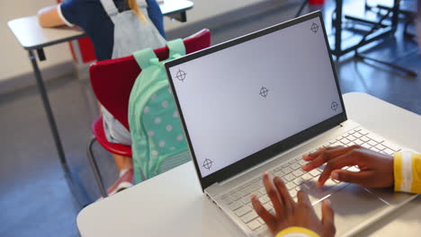 using laptop, student working in school classroom with backpack on chair