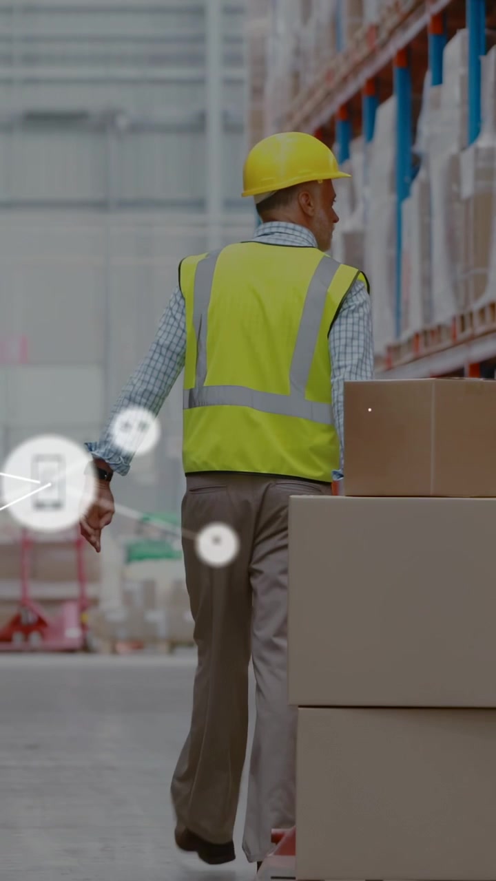Lavoratore con casco giallo e gilet ad alta visibilità cammina lungo il corridoio superando un pallet, mentre appaiono icone di rete.