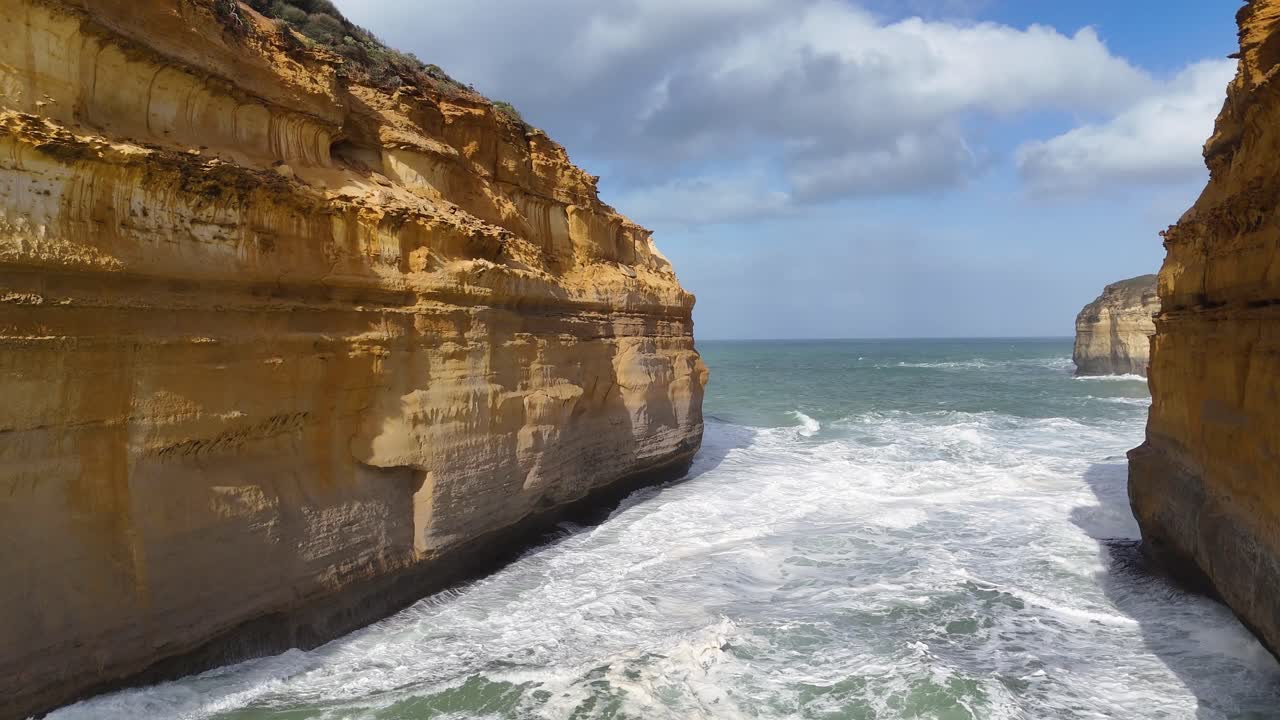 Aerial footage captures dramatic cliffs and ocean waves at Loch Ard Gorge, Port Campbell, under bright daylight