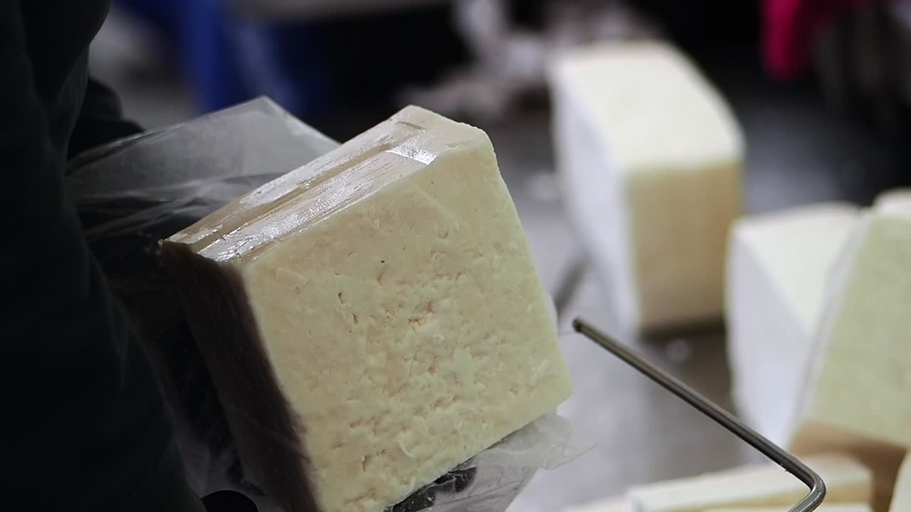 Close-up of Hands Cutting a Block of Fresh Cheese with a Wire Cutter
