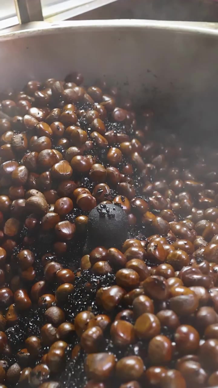 Castagne che arrostiscono in un wok fumante, vista ravvicinata, illuminazione naturale, movimento minimo della telecamera, cibo da strada