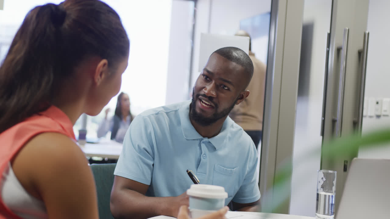 Diverse male and female business colleagues talking and taking notes in office