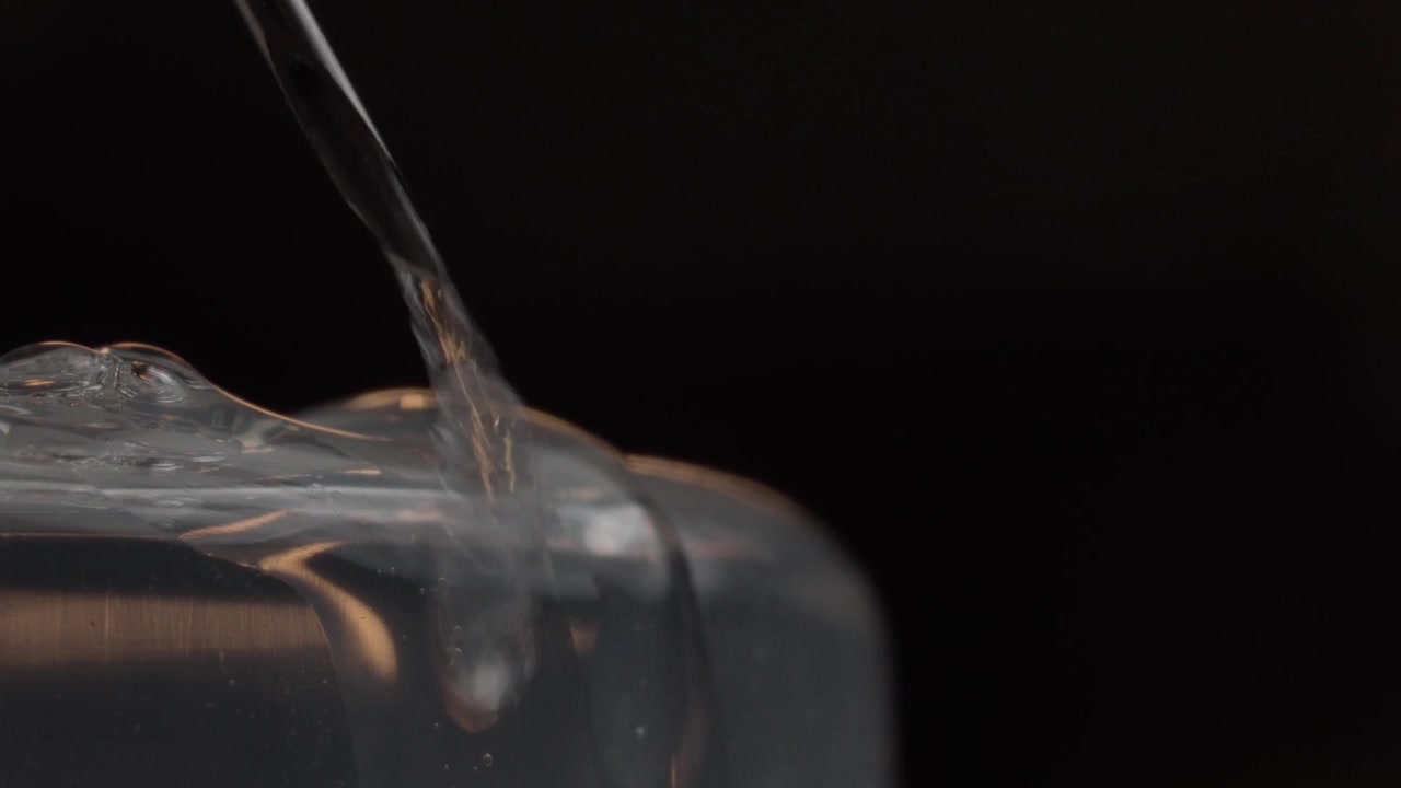 Macro ravvicinata di una goccia di liquido che cade da una pipetta su una superficie di gel cosmetico. Rallentatore che mostra la texture lucida del siero per concetti di cura della pelle, bellezza e laboratorio.