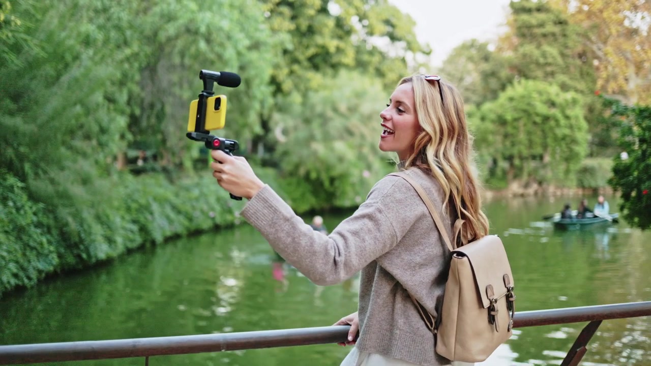 Giovane donna che fa vlogging con lo smartphone in riva a un lago in un parco