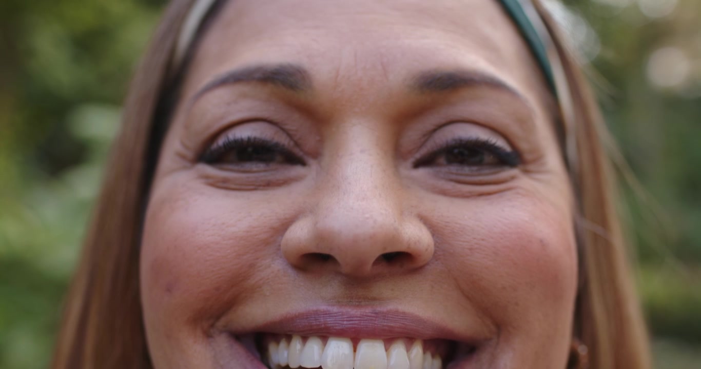 Mujer afroamericana madura con diadema reaccionando a una señal, cambiando de sonrisa a risa y de nuevo a sonrisa en el jardín.