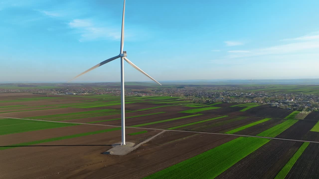 Wind turbine spinning over expansive green fields under a clear blue sky