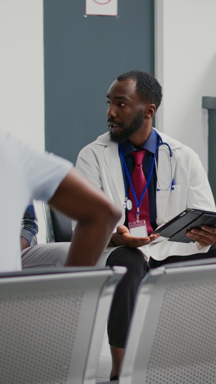 Vertical video: Young medic explaining illness diagnosis to patient in facility reception