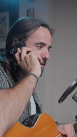 man talking on phone with acoustic guitar and microphone in a studio