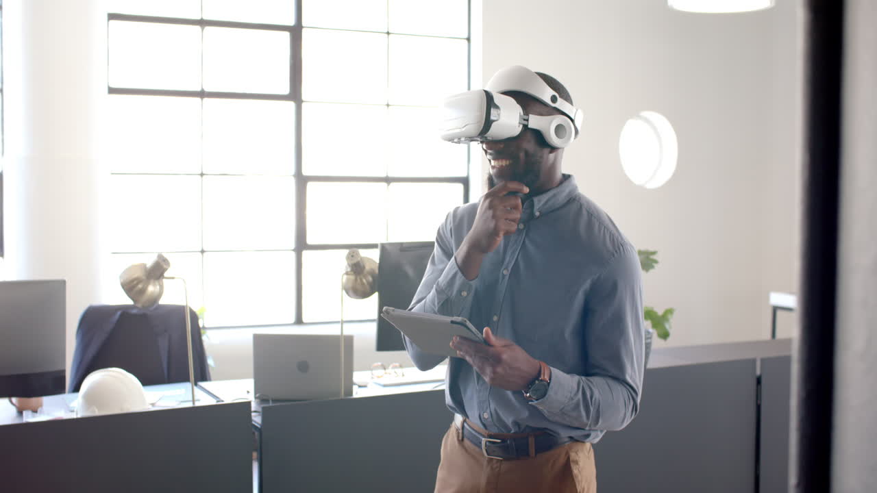 Uomo d'affari che usa un visore VR, tiene in mano un tablet e sorride in un ufficio moderno.
