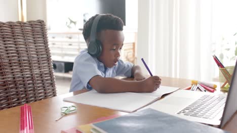 happy african american boy in headphones drawing, using laptop for online class at home, slow motion