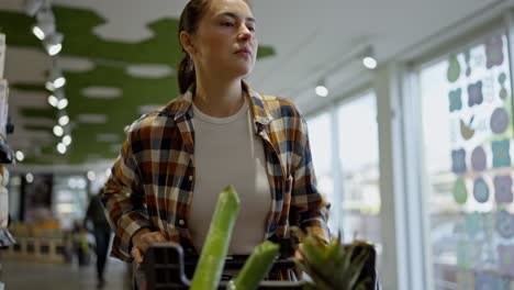 Confident-brunette-girl-in-a-checkered-shirt-chooses-goods-during-her-shopping-with-a-cart-in-a-supermarket