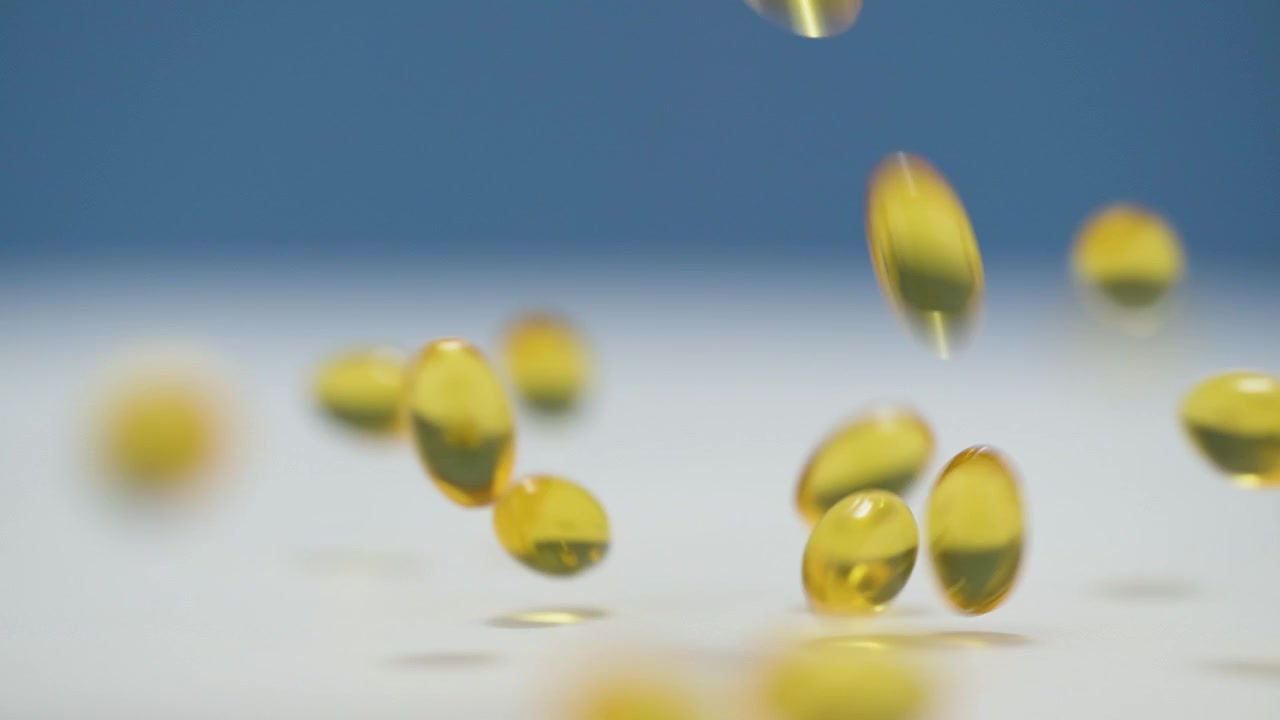 Primo piano di capsule molli gialle che cadono su una superficie bianca con sfondo blu sfocato, Rallentatore
