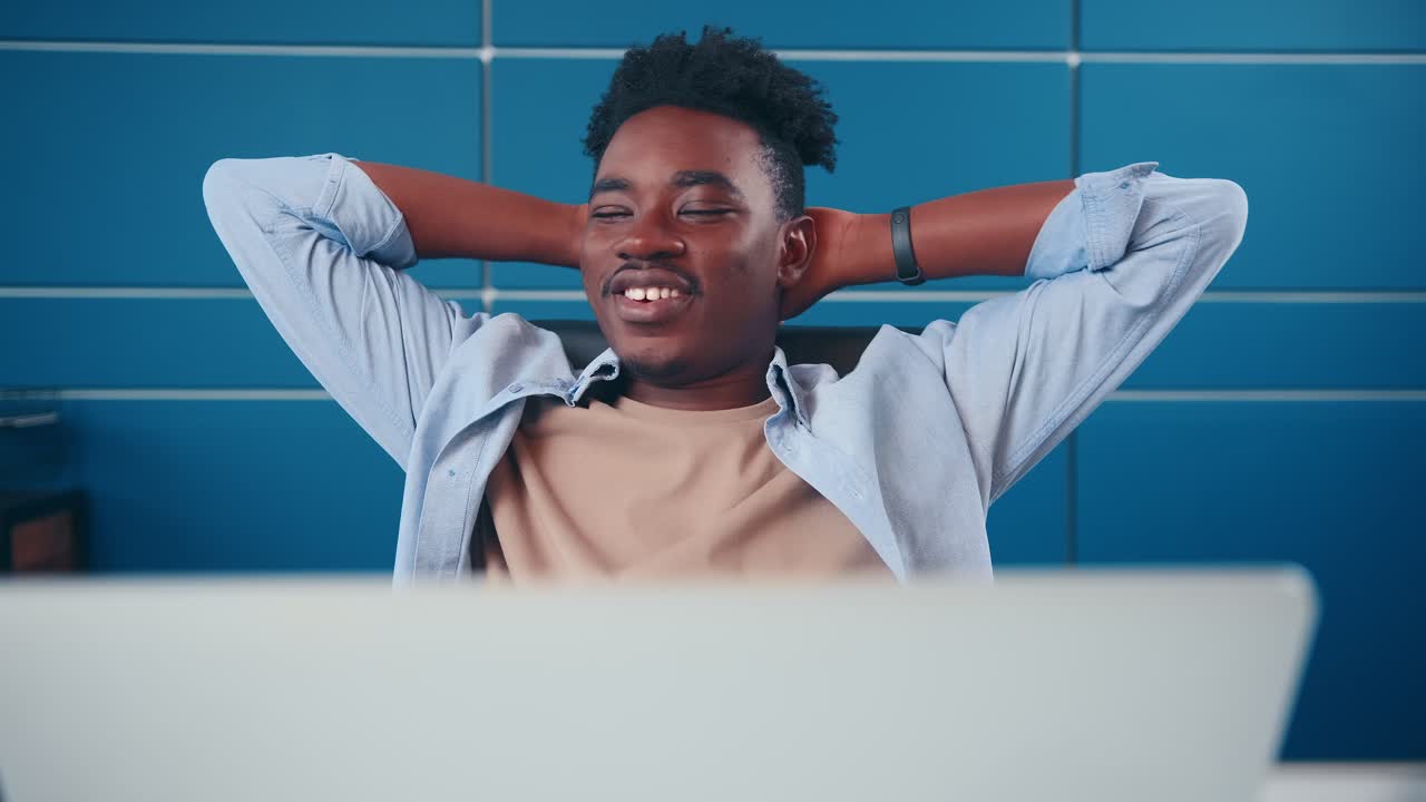 Uomo afroamericano di successo che digita sul laptop e poi si appoggia felicemente allo schienale della sedia.