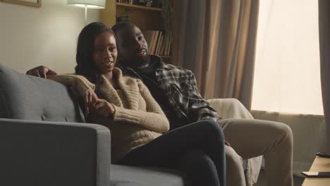 young couple relaxing at home sitting on sofa watching tv together