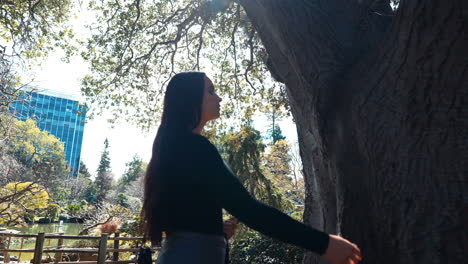 a 4k slow-motion, stabilized video depicting a beautiful young middle eastern female model exploring a lush japanese tea garden slowly moving to touch a tree, peninsula, california