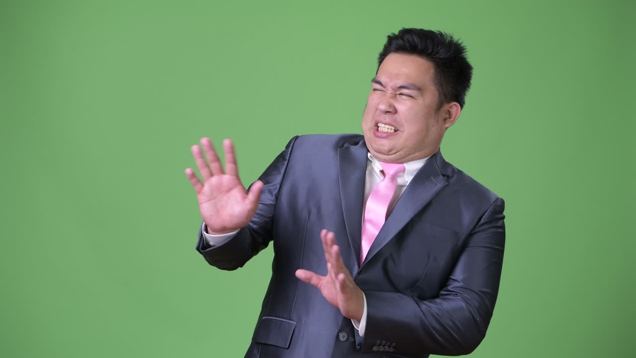 緑色の背景に若いハンサムで肥満のアジア人ビジネスマン