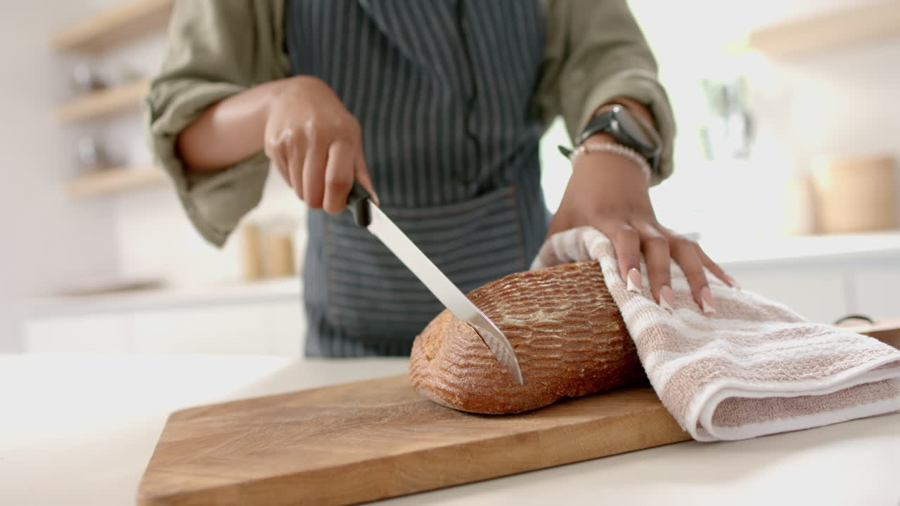 African American young woman wearing apron is slicing bread on wooden board
