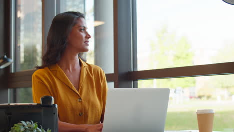 Mature-Businesswoman-Working-On-Laptop-At-Desk-In-Office-Taking-Call-On-Mobile-Phone