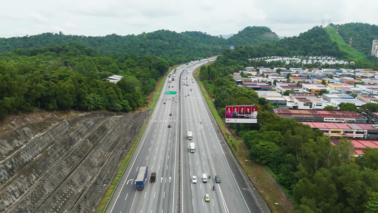 Slow push-in drone shot over a highway in the outskirts of Petaling Jaya, Malaysia. Normal traffic flow running through Malaysian nature.
