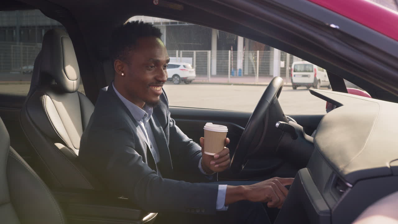 도시 주차장에서 전기 자동차를 운전하는 동안 커피를 마시는 남자