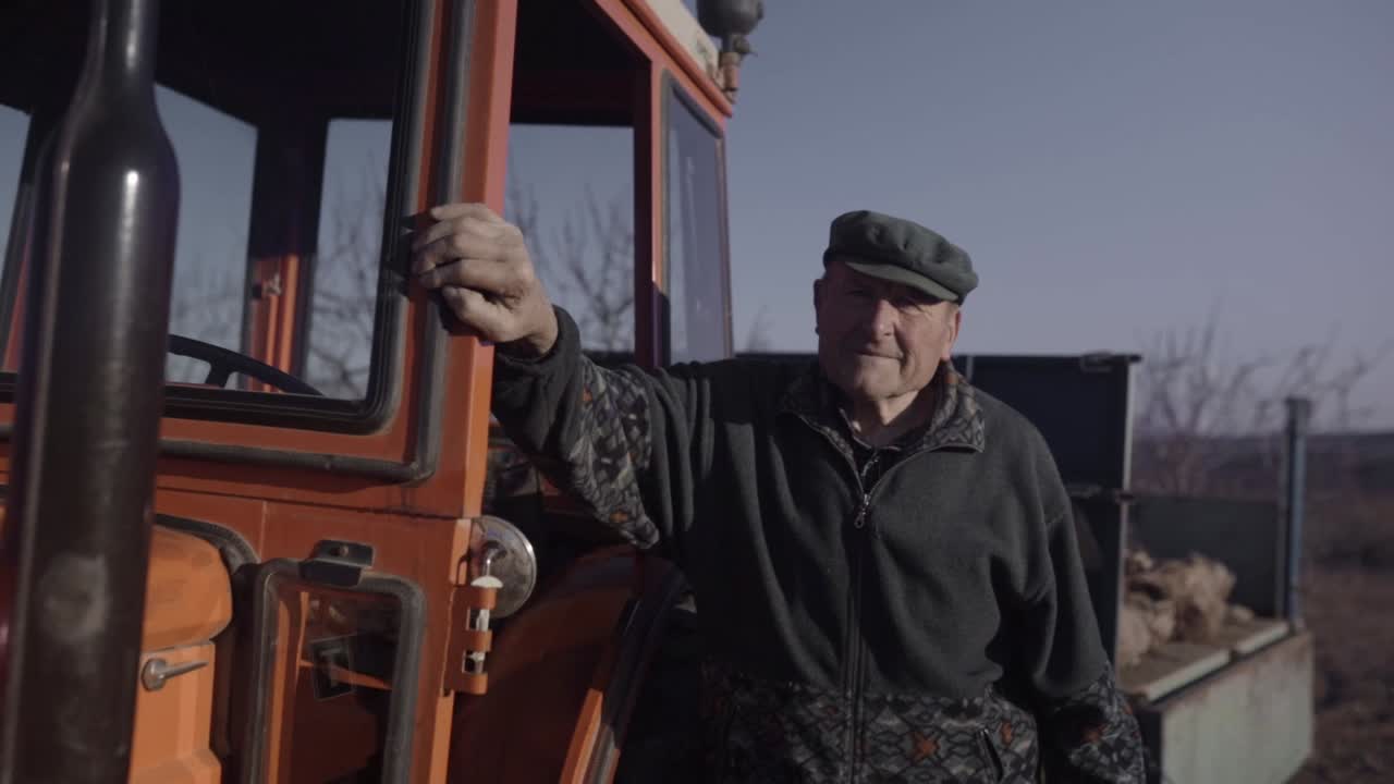 viejo agricultor posando cerca de la cabina del tractor