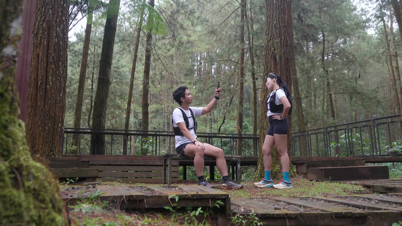 Asian couple taking photo with smartphone during outdoor trail run in Indonesian forest