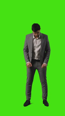 Vertical-Video-Full-Length-Shot-Of-Businessman-Standing-Against-Green-Screen-Straightening-And-Adjusting-Suit-Against-Green-Screen