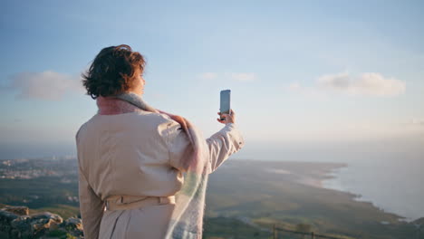 traveler using smartphone recording scenic coastal sunset from high viewpoint